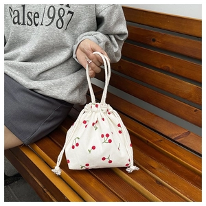 Detail der Cord-Tasche mit Kirschmuster und weißem Seilgriff auf einer hölzernen Sitzbank