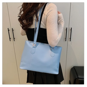 Detail view of light blue tote bag with white contrast stitching and gold metal buckles