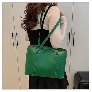 Close-up of green tote bag with white vertical stitching and gold metal hardware detail