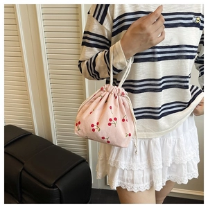 Detail der rosa Cord-Beuteltasche mit Kirschmuster und weißen Baumwollgriffen im Fokus