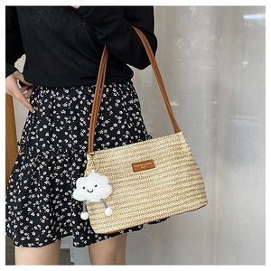 Detail of woven straw tote bag with brown leather tag and cloud plush charm