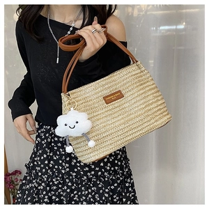 Detail of woven straw tote bag with brown leather handles and a plush cloud charm accessory