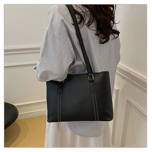 Detail view of black leather tote bag with white contrast stitching on model shoulder