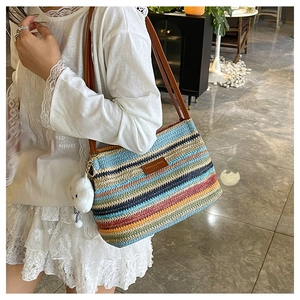 Close-up of a colorful woven tote bag with brown leather handles and a plush charm