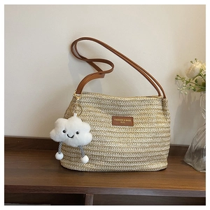 Detail of woven straw tote bag with brown leather strap and white cloud charm