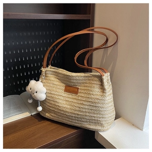 Close-up of woven straw tote bag with brown leather straps and cloud pendant on a table