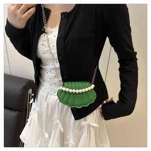 Detail of green shell-shaped crossbody bag with pearl trim and gold chain strap