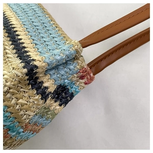 Detail shot of the colorful woven straw tote showing precise brown leather handle stitching