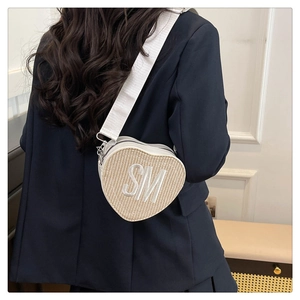Detail of woven heart-shaped crossbody bag with large white SM embroidery on the front