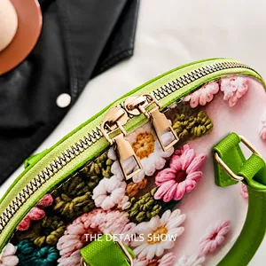 Detail der glatten Doppel-Reißverschlüsse und Blumenstickerei an grüner Handtasche