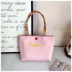 Detail of pink canvas tote featuring colorful woven handles and embroidery