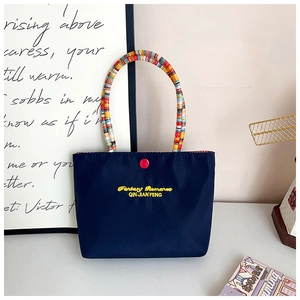 Detail of navy nylon handbag featuring colorful braided handles and yellow embroidery