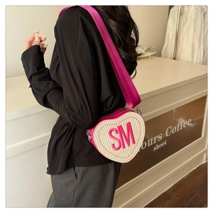 Détail du sac bandoulière tissé en forme de cœur avec broderie SM rose sur un modèle