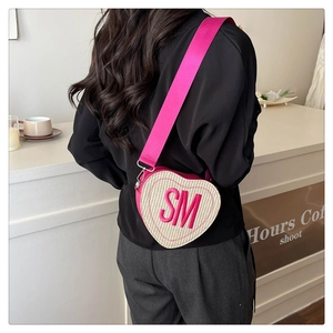 Detail of pink heart-shaped woven crossbody bag with SM embroidery worn by a model