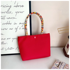 Detail of red tote bag featuring vibrant rainbow braided handles and snap button closure