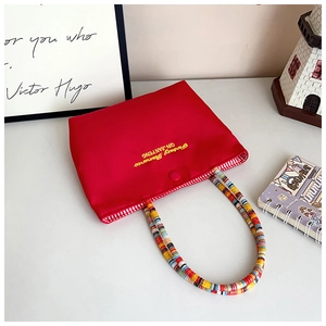 Detail of red fabric handbag featuring yellow embroidery and colorful woven handle