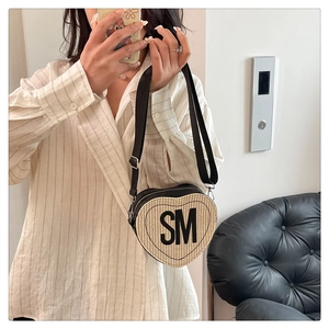 Détail du sac en paille en forme de cœur avec lettrage SM et bandoulière noire