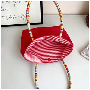 Modern red tote bag with colorful braided handles and striped lining on white desk