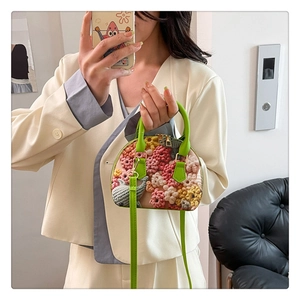 Details einer bunten Häkel-Handtasche mit grünen Griffen und goldenem Reißverschluss