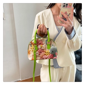 Detailaufnahme von 3D-Blumenstickerei und grünem Ledergriff an einer muschelförmigen Tasche