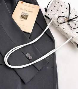 Détail du sac blanc en tissu texturé avec imprimés oiseaux et nœud sur un blazer gris chic