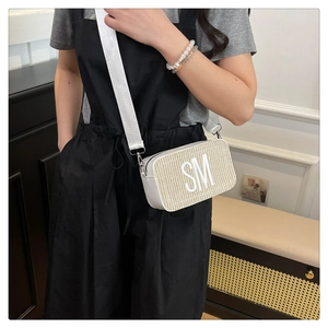 Detail der beigen geflochtenen Umhängetasche mit weißem SM-Patch und breitem Gurt