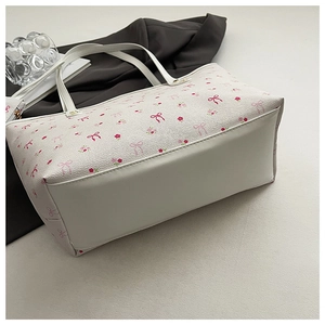 Détail d'un cabas blanc avec motifs floraux, nœuds rouges et coutures de la base