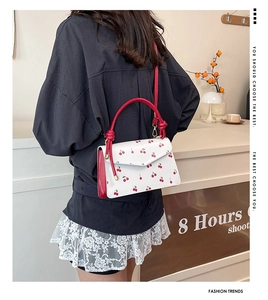 Detail showing red cherry print on white leather bag with red knotted handle decorations