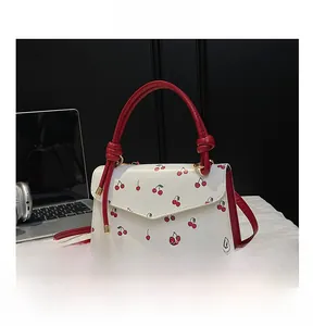 Detailed close-up of a white leather crossbody bag with red cherry prints and woven handle