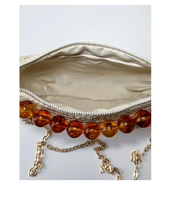 Detail of straw woven bag featuring amber beads, fabric lining, and a gold metal chain strap