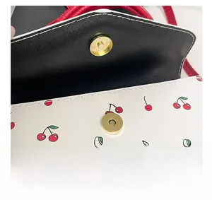 Detail of golden magnetic snap closure and cherry pattern on white leather crossbody bag