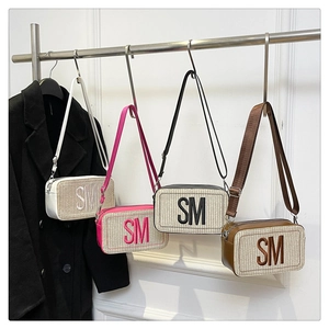 Gewebte Umhängetaschen mit SM-Stickerei in Weiß, Rosa, Schwarz und Braun an einem Ständer