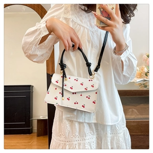 Detail view of white small square handbag featuring cherry prints and black handle