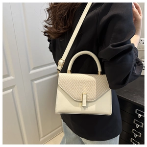 Detail view of a white crossbody bag with beige woven flap and gold hardware on a model