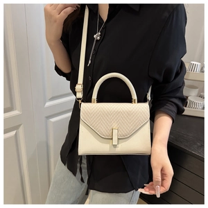 Detail of cream leather and straw textured flap on a crossbody bag shown on a model