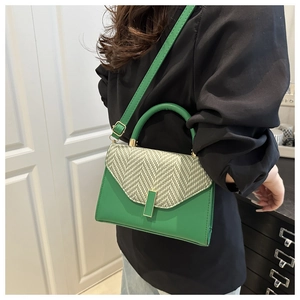 Close-up of green leather handbag with herringbone weave flap and gold twist lock