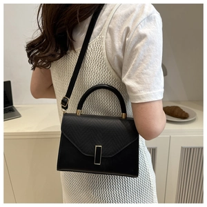 Detail of black crossbody bag featuring textured lizard skin flap and golden hardware