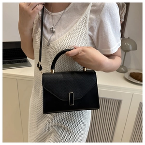 Detail of a chic black leather crossbody bag with a gold buckle and textured flap