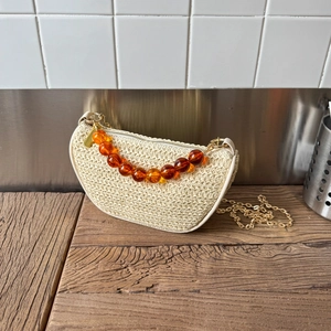 Sac demi-lune en paille tressée avec perles ambrées et chaîne dorée sur bois