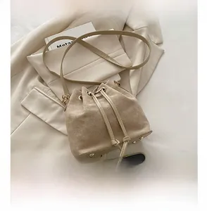 Detail view of beige drawstring bucket bag with gold studs and phone for size reference