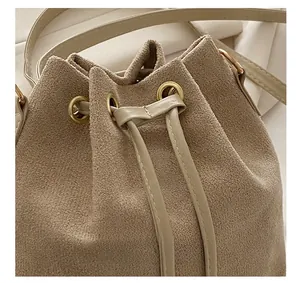 Detail view of beige suede bucket bag with drawstring closure and golden metal eyelets