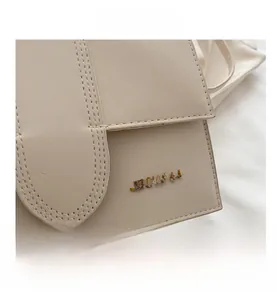 Gros plan sur la texture du cuir beige et le logo doré de ce sac bandoulière élégant
