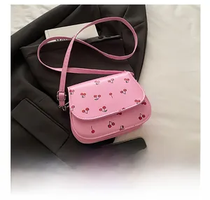 Detail of pink saddle bag with cherry print, adjustable strap and silver metal buckle
