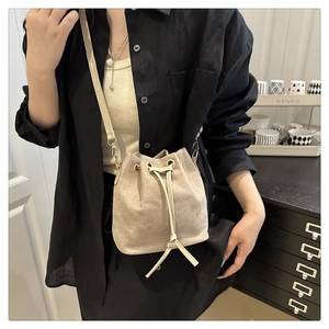 Detail of a beige canvas bucket bag with drawstring closure and golden hooks