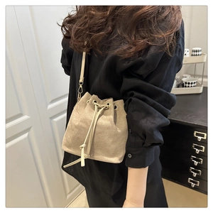 Close-up of a beige suede drawstring bucket bag worn by a model in a minimalist home setting