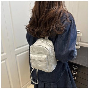Rear view of model wearing a mini silver metallic backpack with small front zip pocket