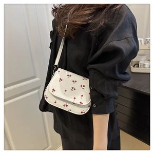 Detail of white cherry print saddle bag with slim strap and sleek metal closure