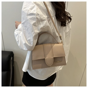Détail du sac à rabat beige avec logo doré et bandoulière réglable porté par le mannequin