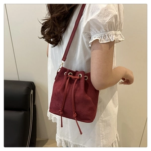Macro view of burgundy faux suede bucket bag featuring drawstring closure and gold hardware