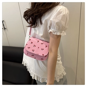 Close-up of a pink saddle bag featuring red cherry prints and a slim leather strap
